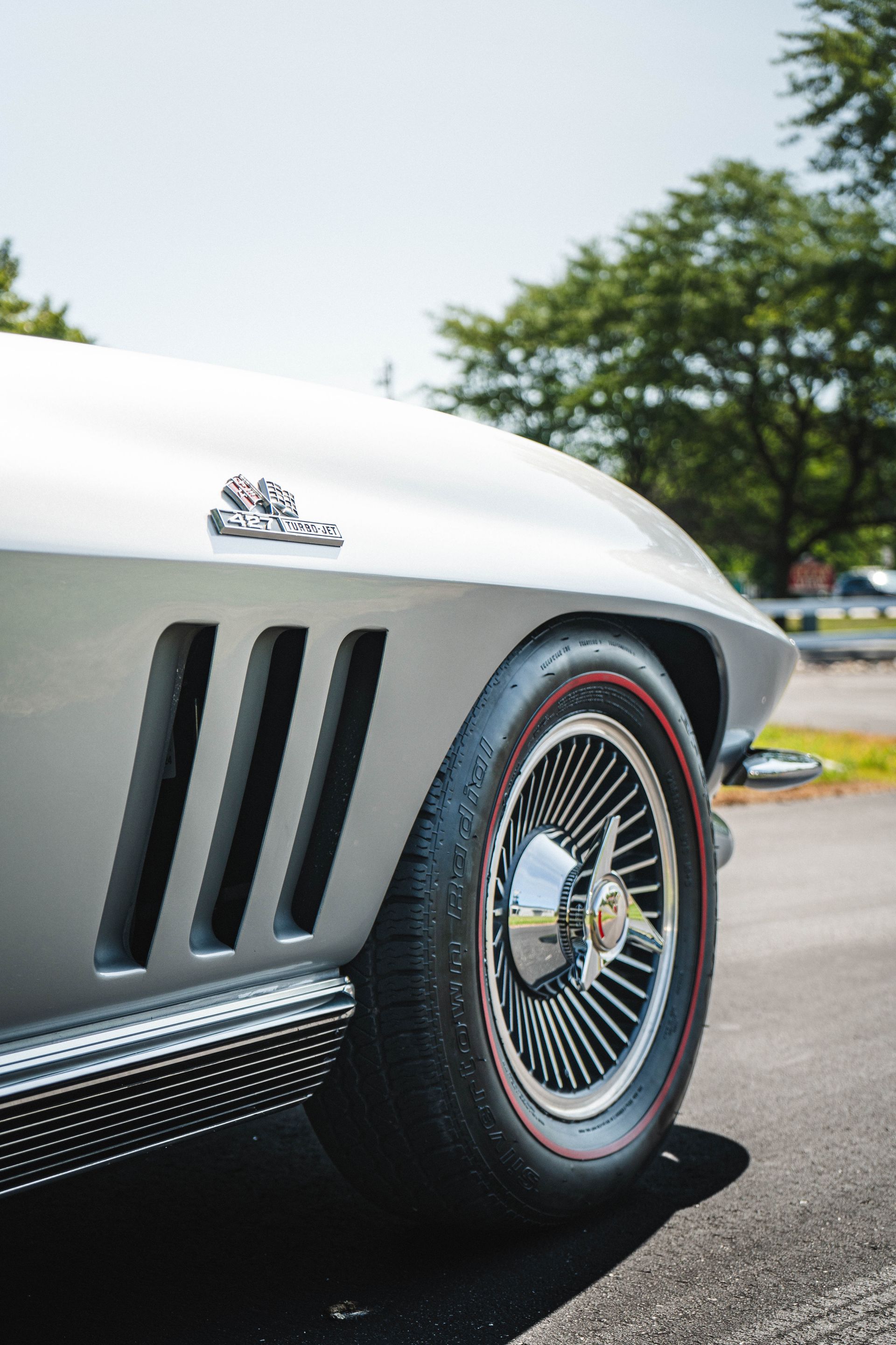 Silver vintage Corvette with side vents and wire wheels.