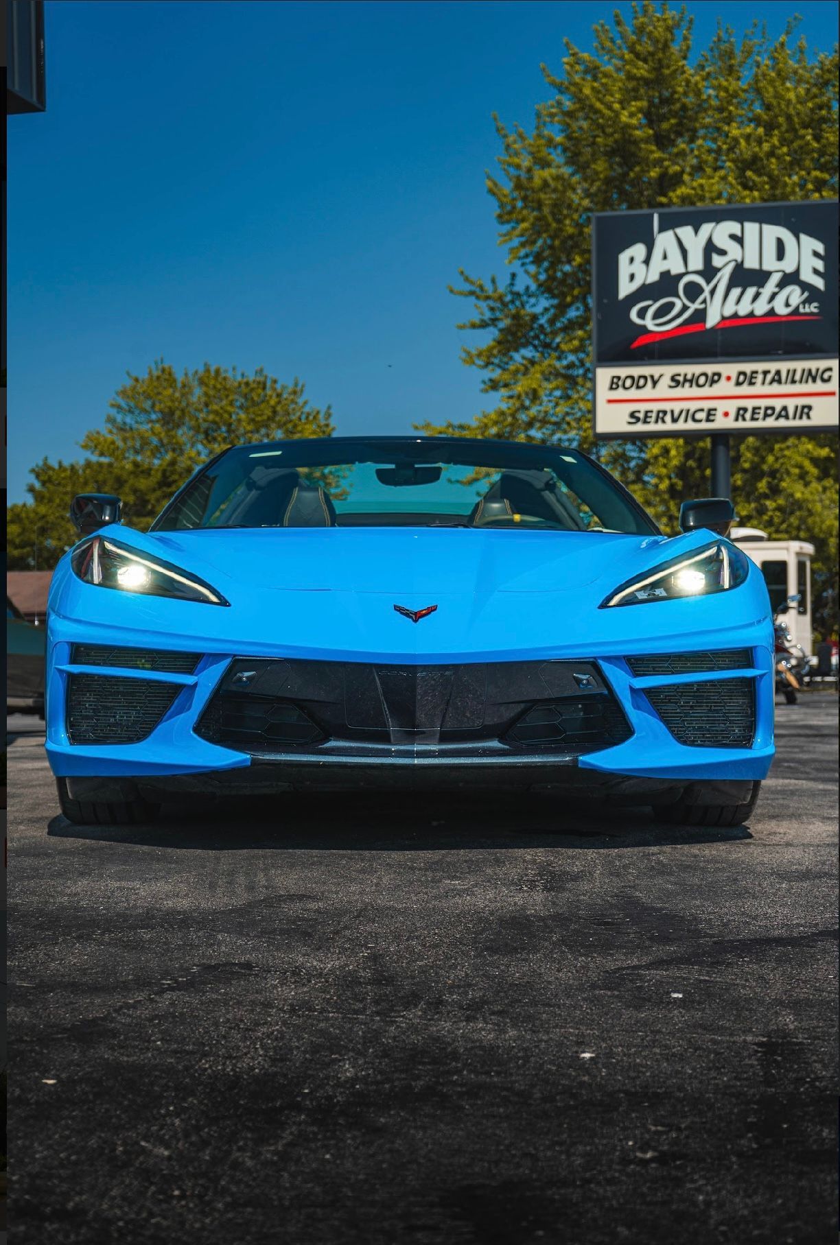 Blue Corvette sports car parked in front of Bayside Auto shop sign on a sunny day.