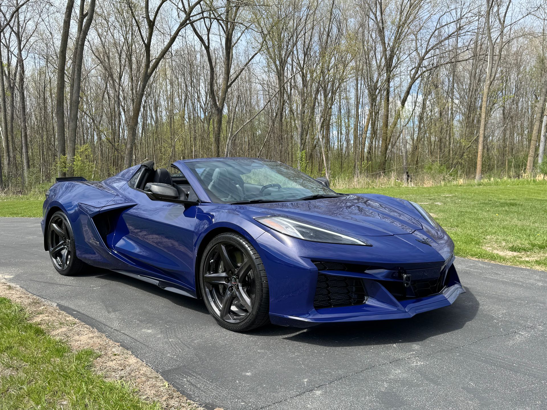 Blue sports car parked on a paved driveway in a wooded area.