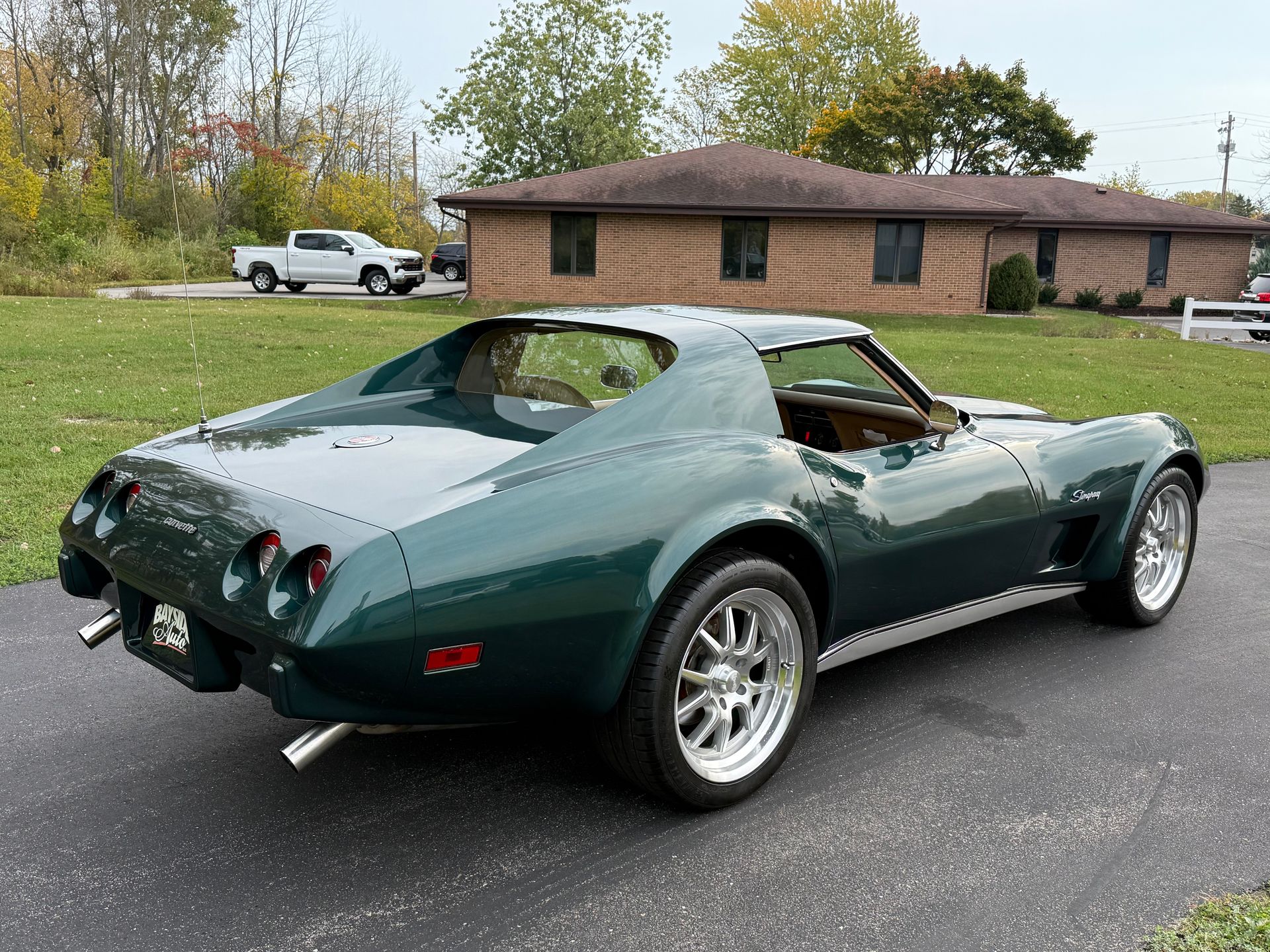 Green classic Corvette on a paved driveway in front of a brick building.