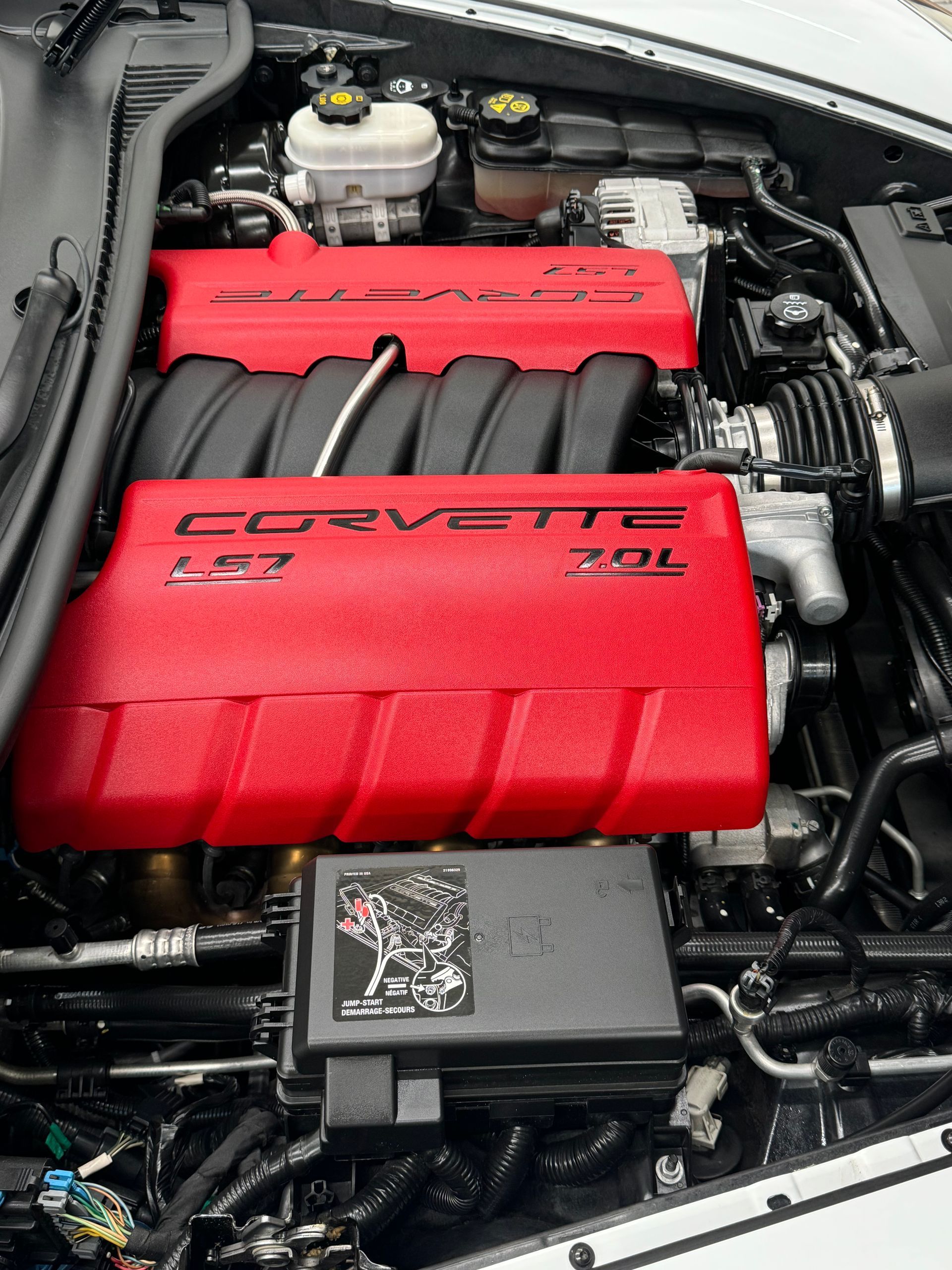 Red engine cover of a Corvette, visible in the car's engine compartment. Black and silver components surround it.