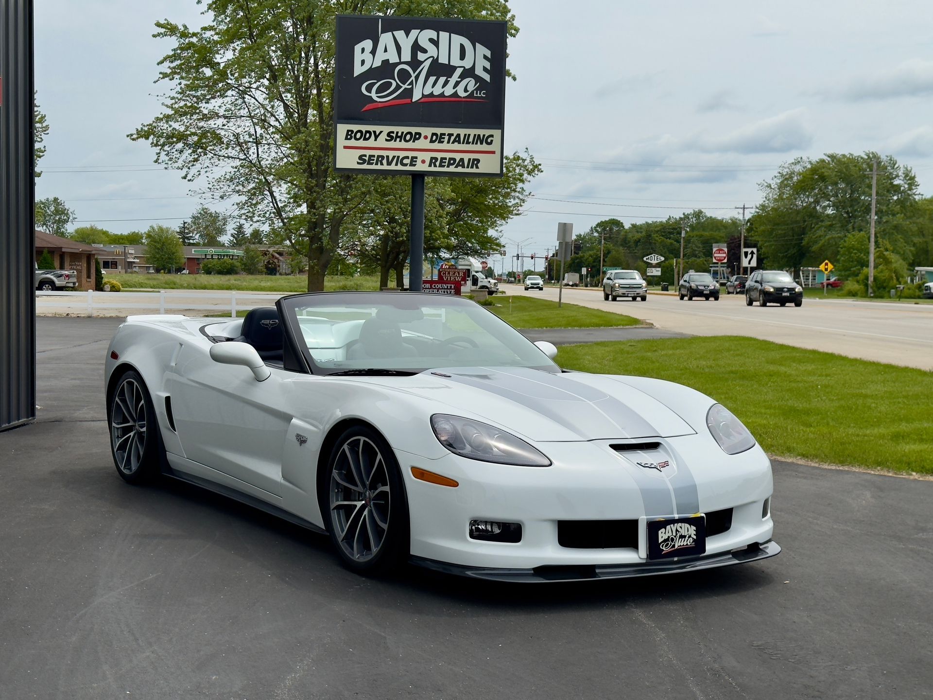 White Corvette convertible parked in front of a Bayside Auto sign on a sunny day.