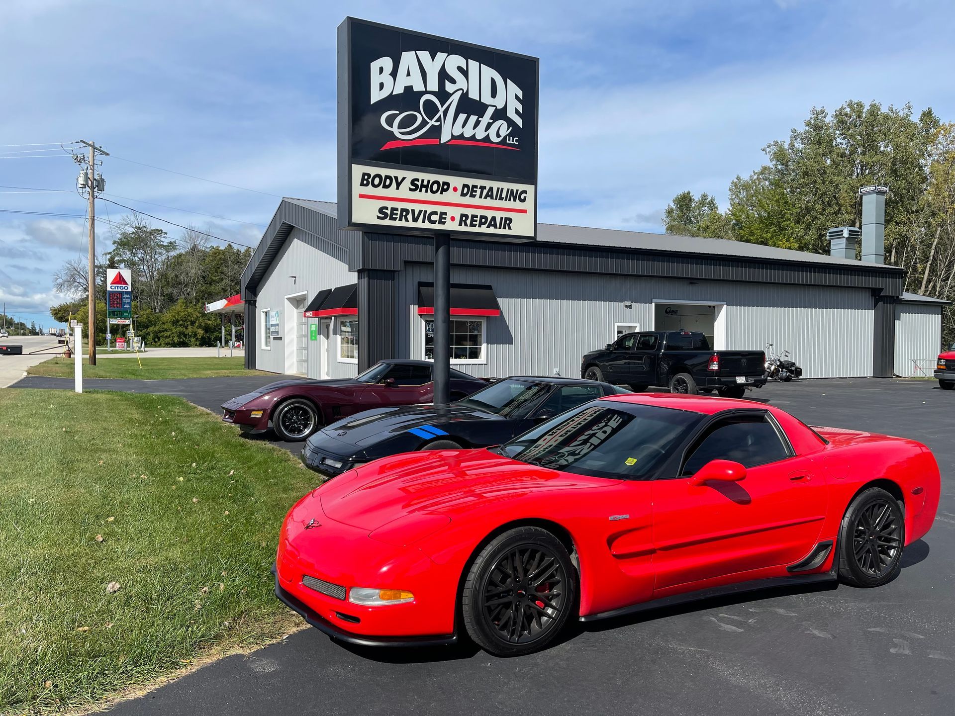 Red Corvette parked in front of Bayside Auto, with two other cars; building has sign,