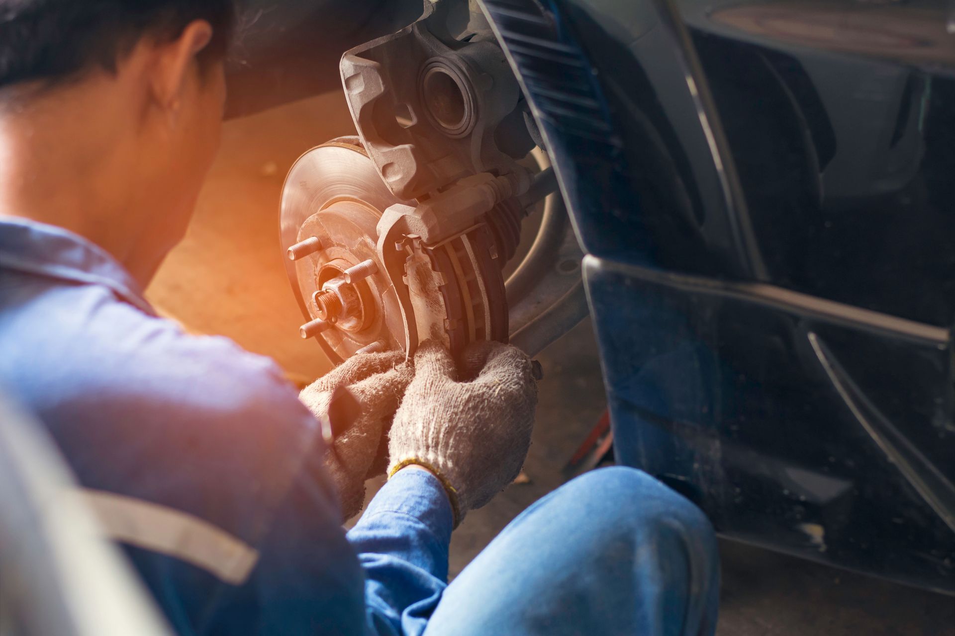 A man is kneeling down fixing a brake pad on a car.