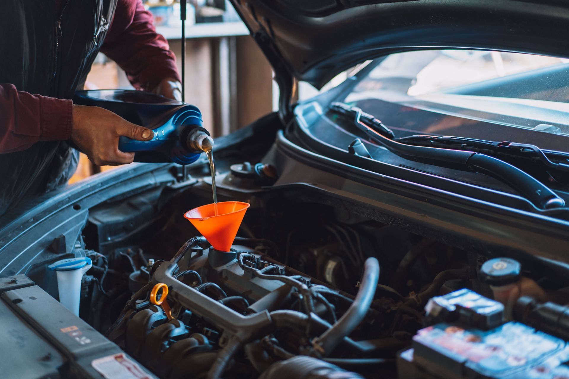 A man is pouring oil into the engine of a car.