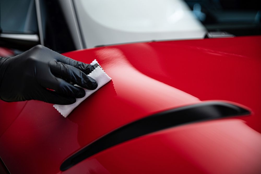 Person wiping the front of a copper-colored car with a microfiber cloth, near the headlight.
