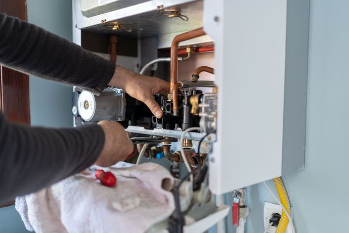 A man is fixing a boiler with a wrench and a towel.