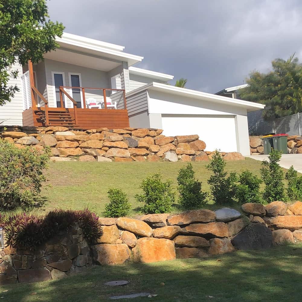 Rock Retaining Wall Leading To White Home — Retaining Wall Builders in Northern Rivers, NSW