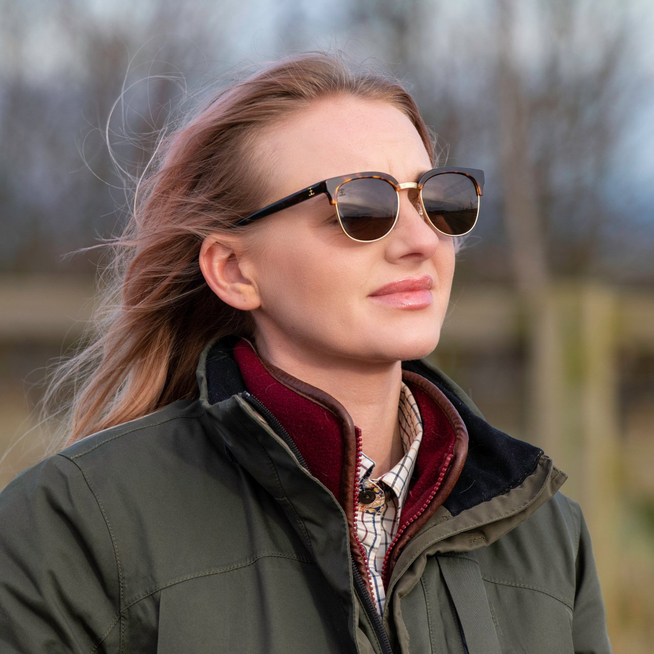 Person wearing sunglasses and a dark jacket outdoors on a windy day