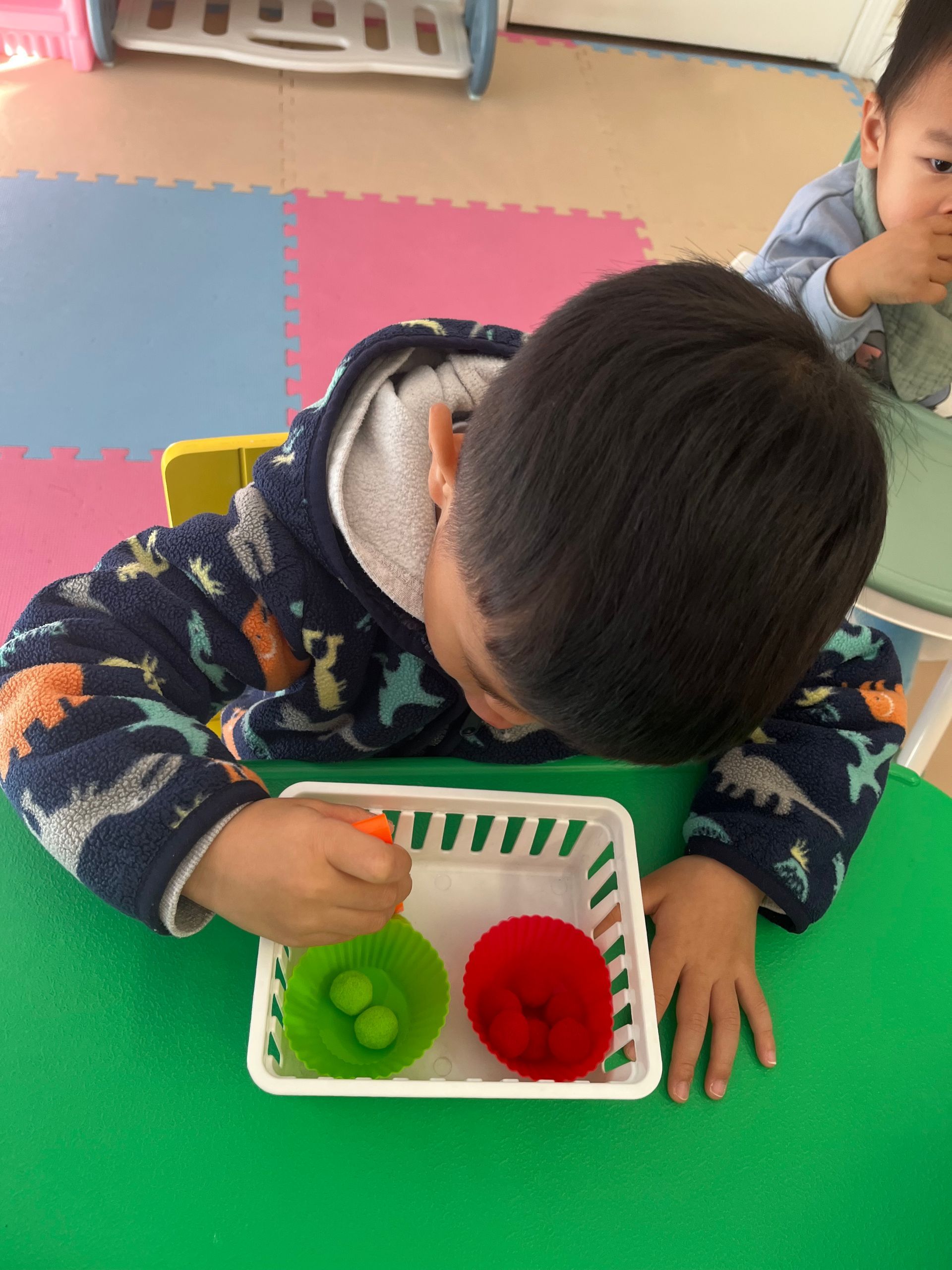 Child interacting with green and red objects in a white basket on a green table.