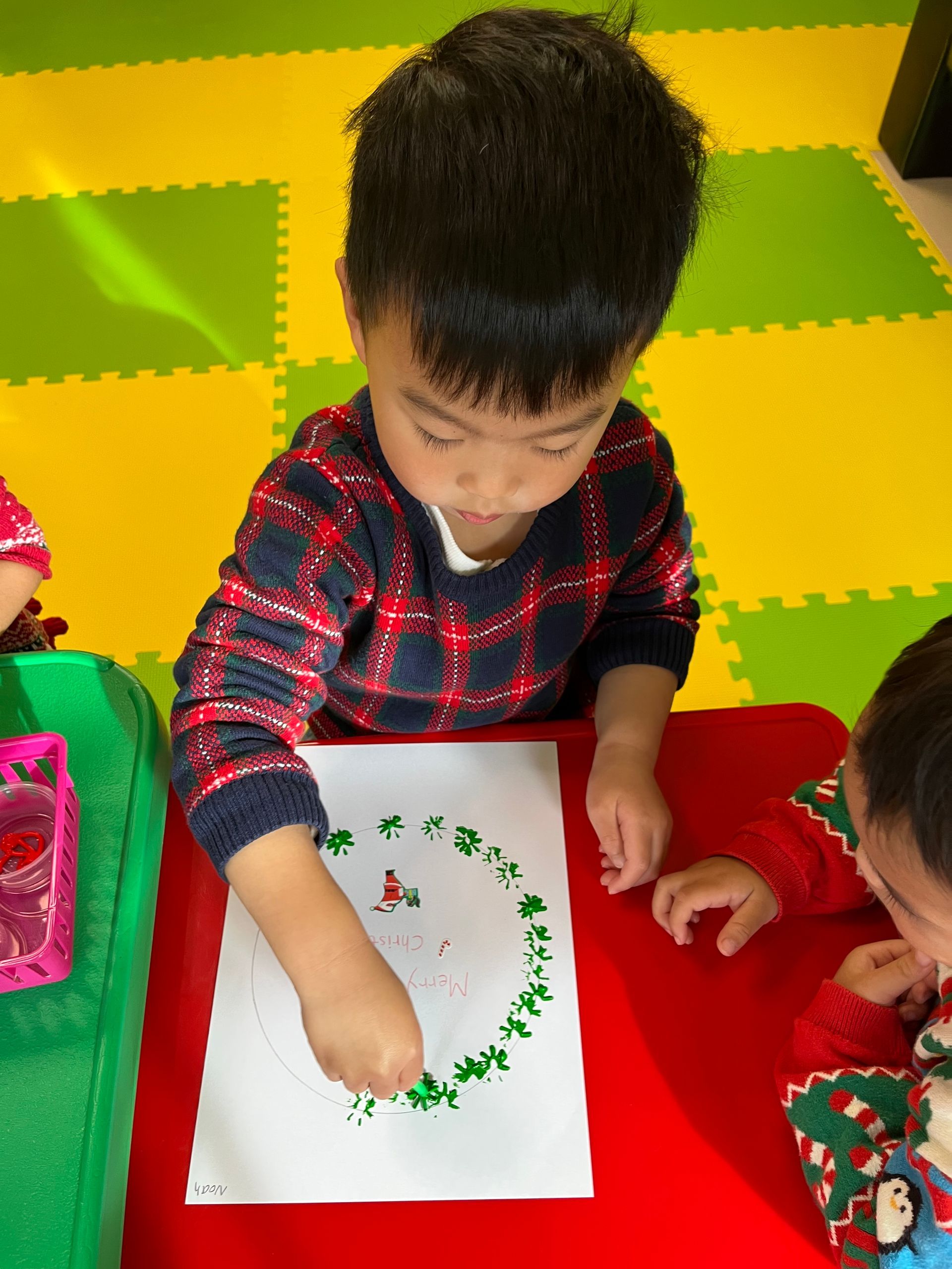 Boy painting green around a circle on paper at a red table.