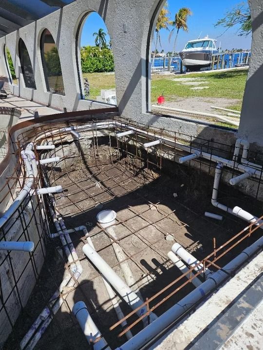 Empty pool under construction with exposed rebar, white pipes, and marina boats in the background