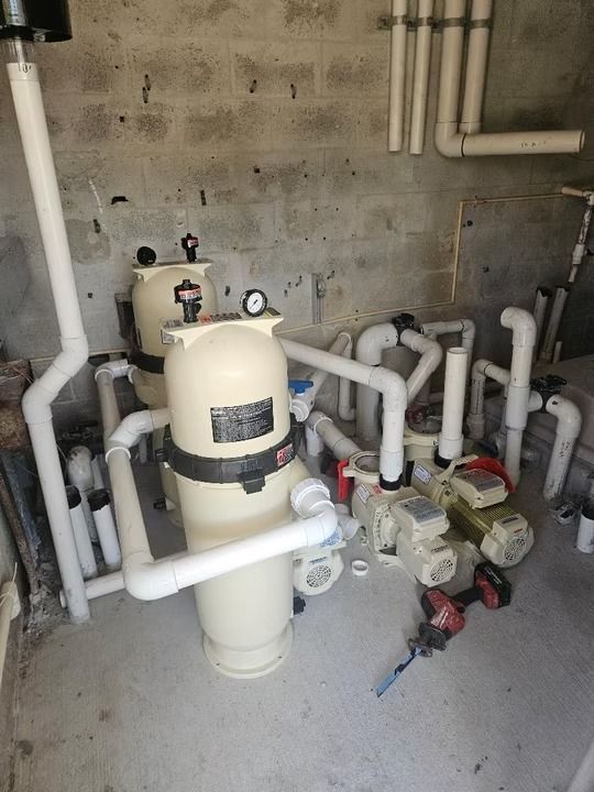 Basement utility room with white pipes, pumps, and a beige water filtration tank on a concrete floor