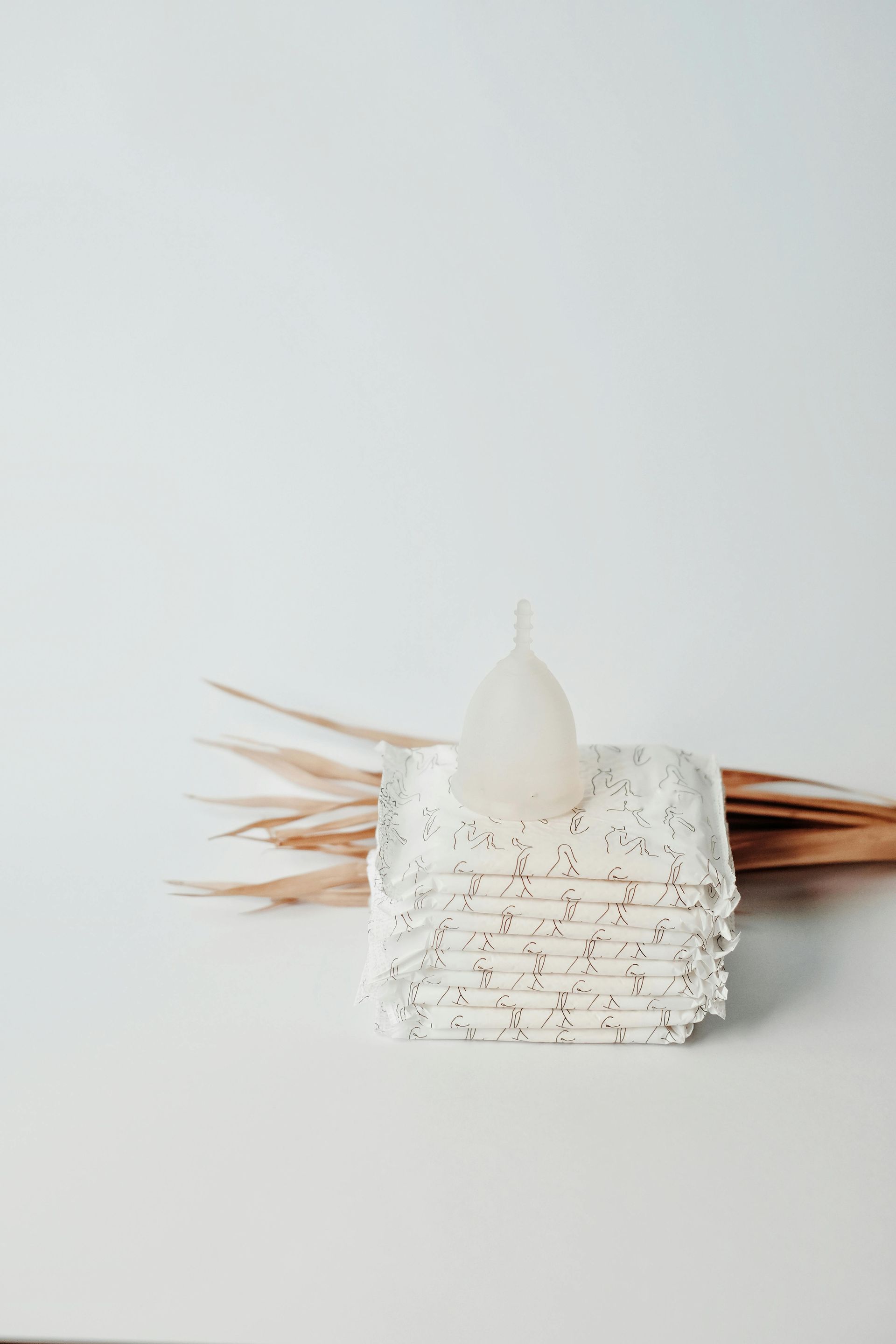 White tiered candle holder with a small candle and dried reeds against a light gray background