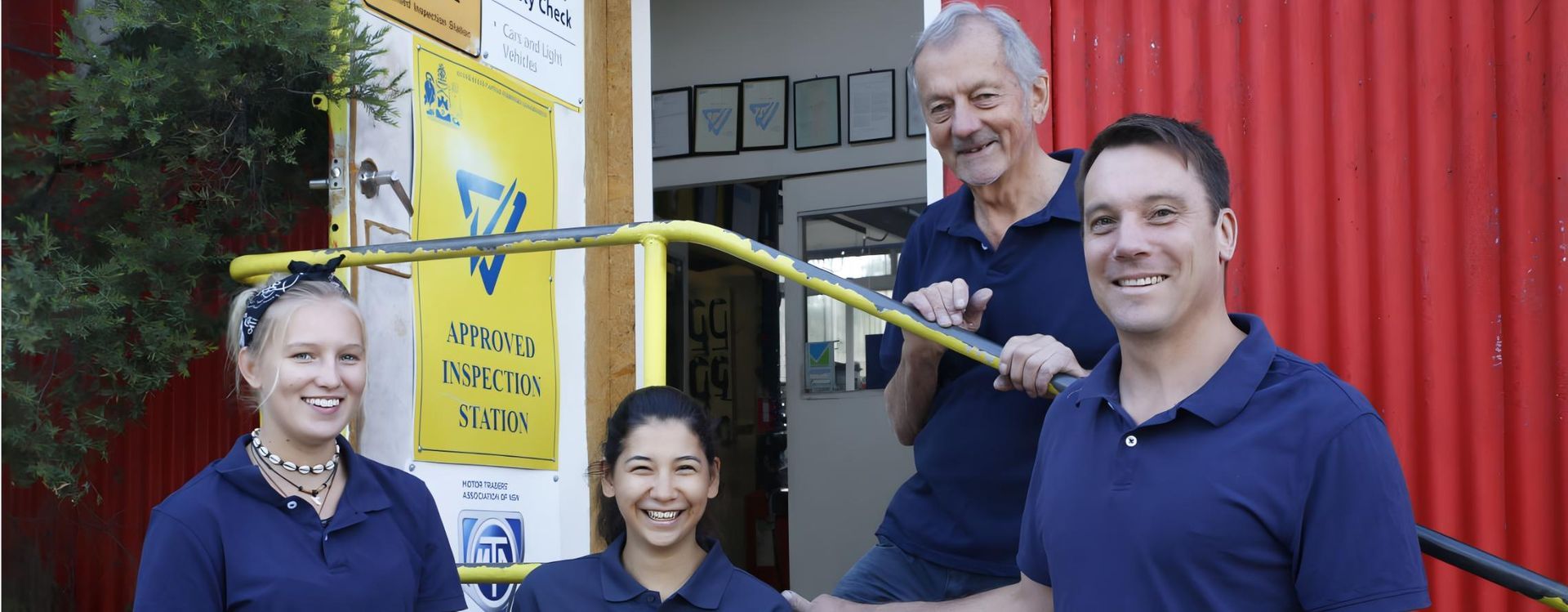 A Group of People Standing Next to Each Other in Front of a Red Wall — CWC Auto Services In Ainslie, ACT