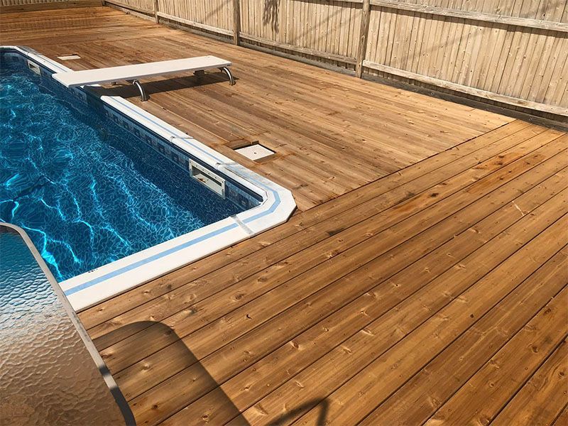 Wooden deck surrounding a blue swimming pool with a diving board.