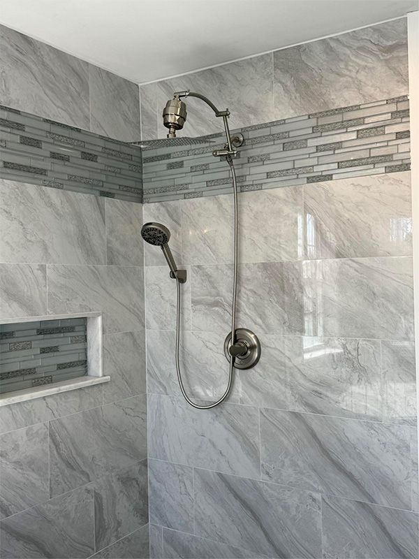 Gray tiled shower with a decorative mosaic tile stripe and silver shower fixtures.