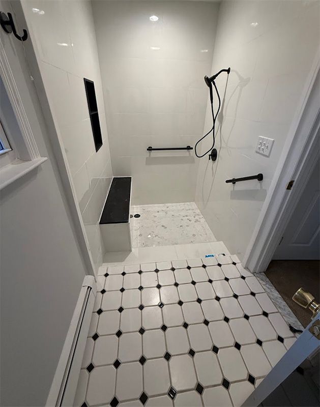 Accessible shower with black grab bars, showerhead, and black and white tile flooring.