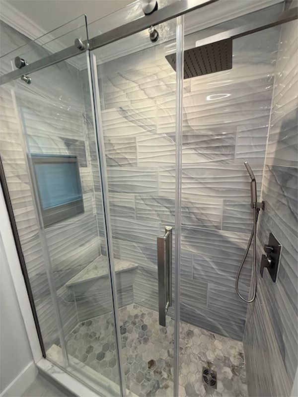 Glass-enclosed shower with gray and white textured tile, a built-in seat, and a rainfall shower head.