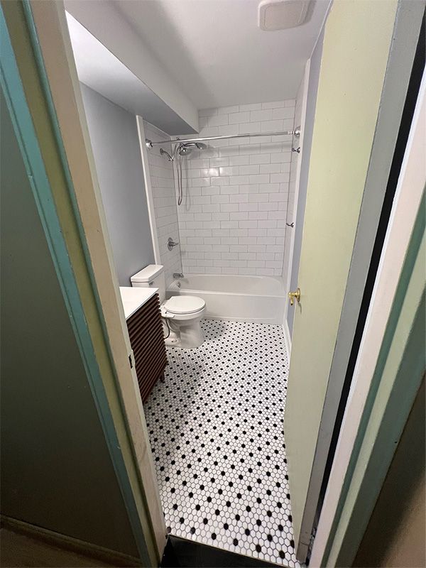 Bathroom with black and white patterned floor, white subway tile shower, and wood vanity.