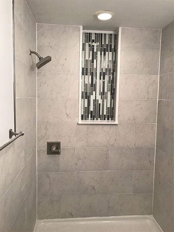 Shower with gray tile, mosaic accent, and showerhead. Recessed shelf with a light.