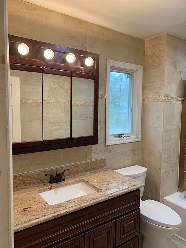 Bathroom with brown vanity, granite countertop, tiled walls, mirror cabinet, and a white toilet.