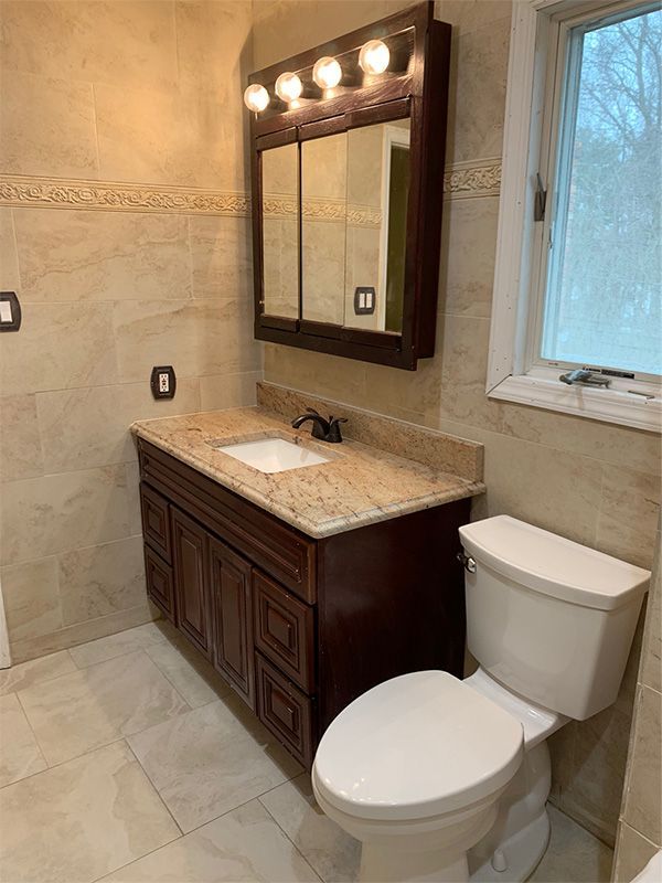 Bathroom with dark wood vanity, light stone tile, and a toilet.