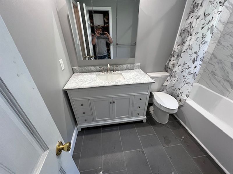 Bathroom with gray walls, vanity, toilet, tub/shower, and gray tile floor.