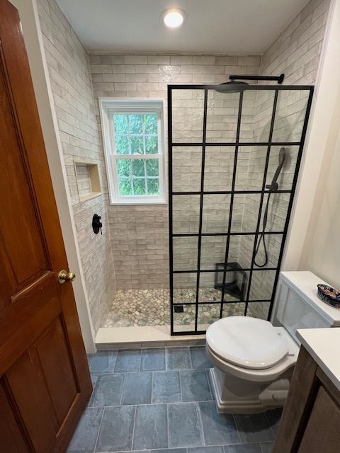 Small bathroom with glass shower enclosure, stone floor, and light brick tile.
