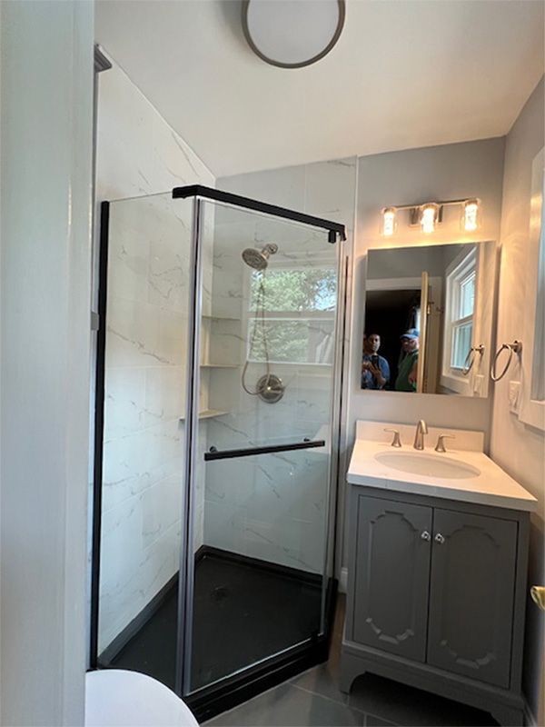 Bathroom with a black-framed glass shower, gray vanity, and white walls.