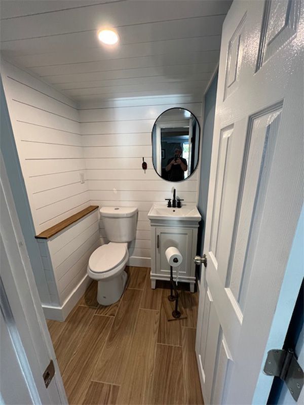 Small bathroom with shiplap walls, toilet, vanity, and a black mirror.