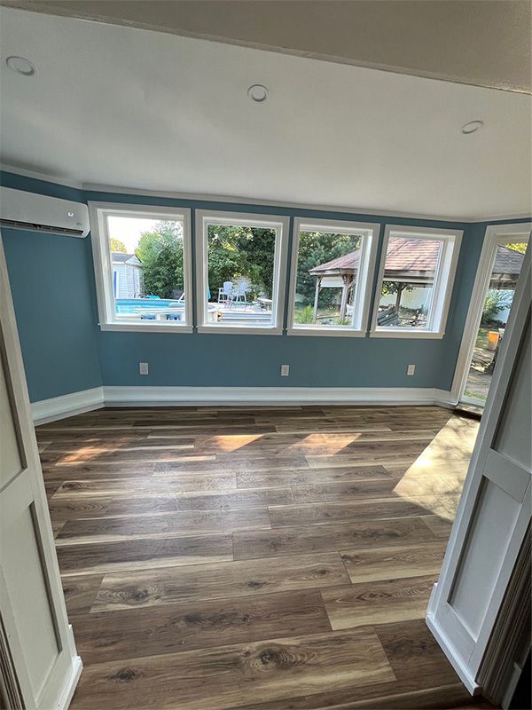 A room with blue walls, many windows, wood-look floor, and open white doors.