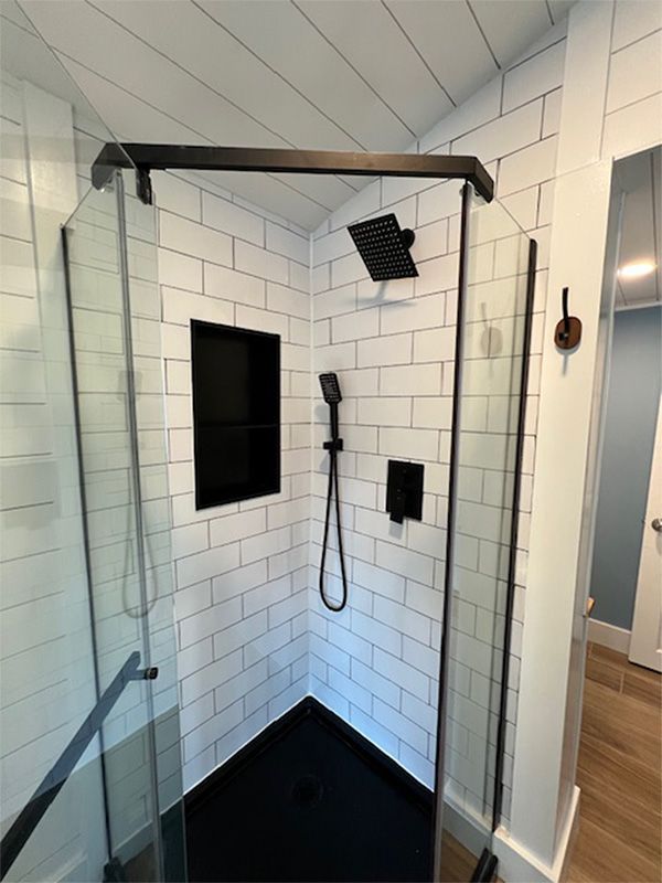 Black-framed, glass-enclosed shower with black fixtures and black tile base, against white subway tile walls.