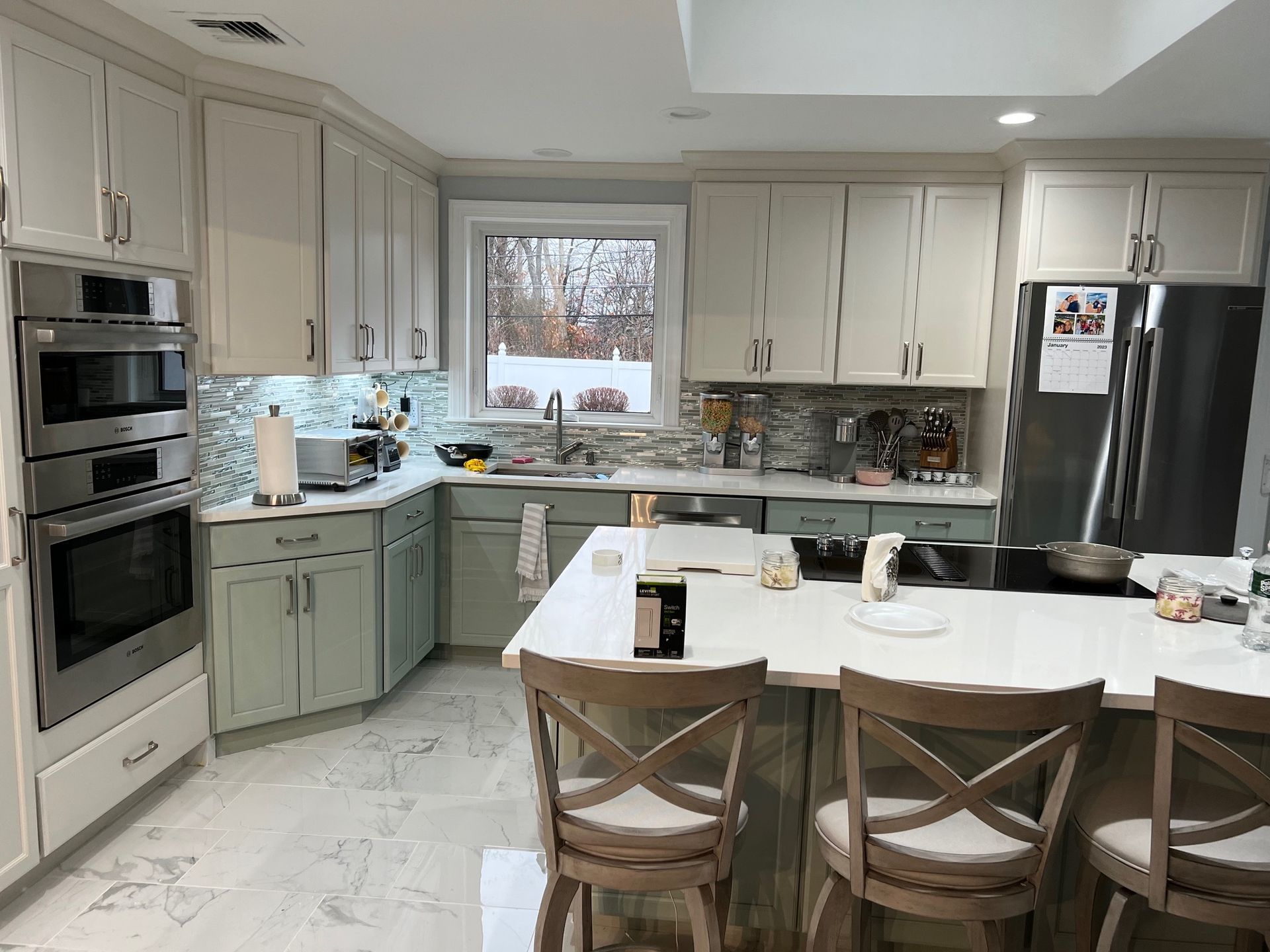 Kitchen with white and green cabinets, stainless steel appliances, and a central island with bar stools.