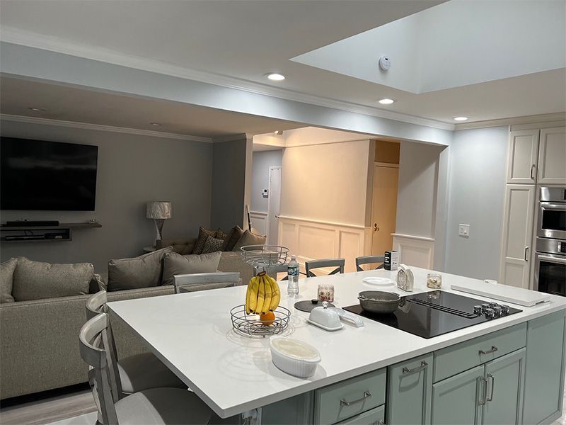 Kitchen with a large island, connected to a living area with couches and a TV. Blue cabinets and light gray walls.
