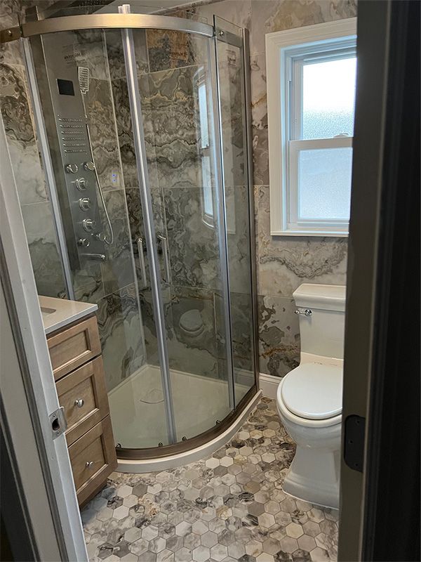 Bathroom with glass shower, toilet, vanity, and hexagon tile floor. Gray and beige tones dominate.