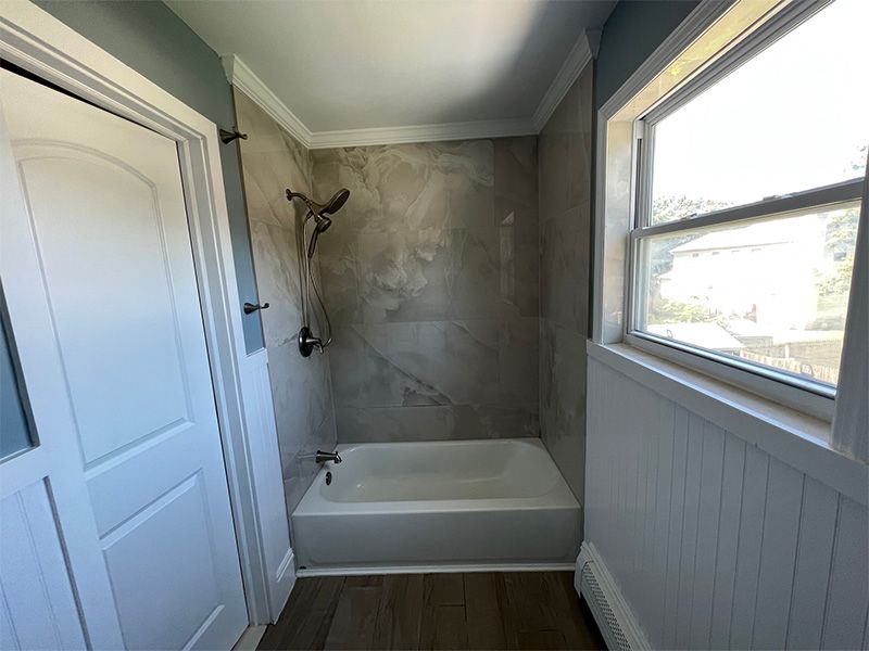 Bathroom with a tub and showerhead, light walls, and a window.