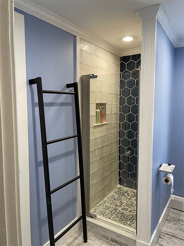 Bathroom with a shower; blue walls, black ladder, glass door, and hexagon tiles.