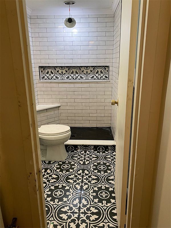 Bathroom with patterned floor, white brick shower walls, and a recessed shelf.