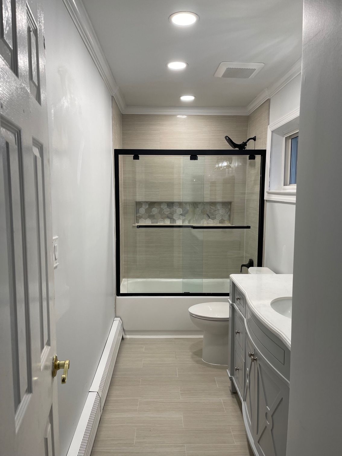 Bathroom with light-colored tile, a white toilet and vanity, and a glass shower door with a black frame.