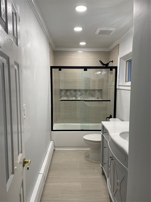 Bathroom with gray tile, white walls, black shower frame, and vanity.