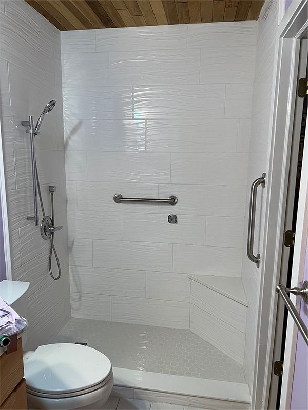 Accessible white-tiled shower with built-in bench, grab bar, and hand shower.