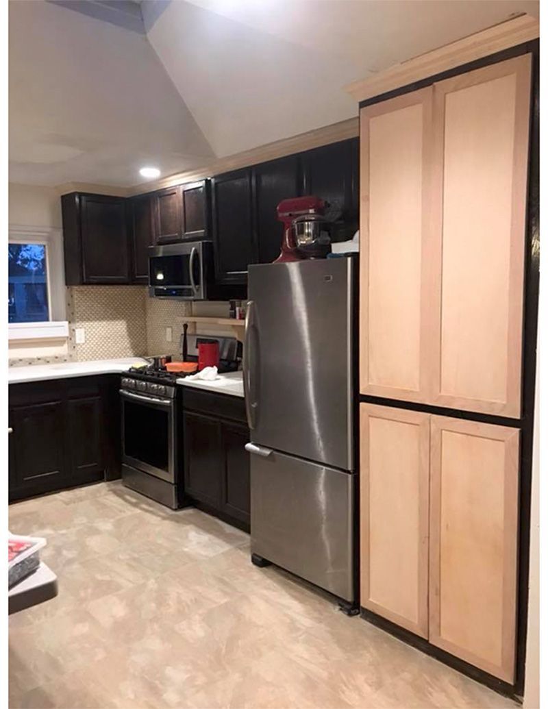Kitchen with stainless steel refrigerator, brown cabinets, stove, microwave, and light wood storage cabinets.