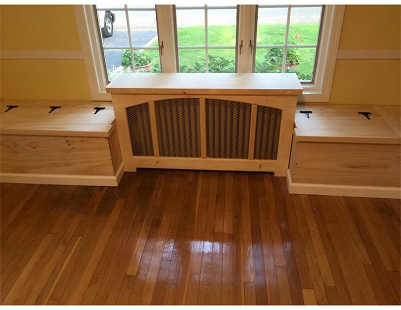 Wooden window seat with storage benches on either side, centered on a window with a radiator cover.