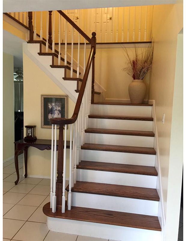 Wooden staircase with white risers and brown treads. Beige walls, a table, and a vase are also visible.