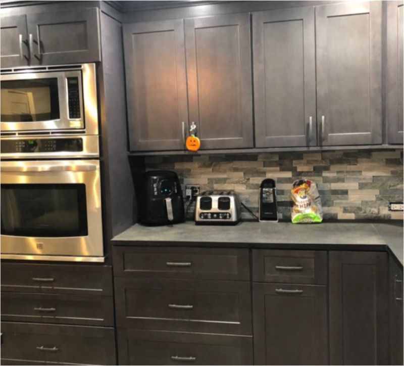 Gray kitchen cabinets with a built-in microwave and oven, countertop appliances, and a tiled backsplash.