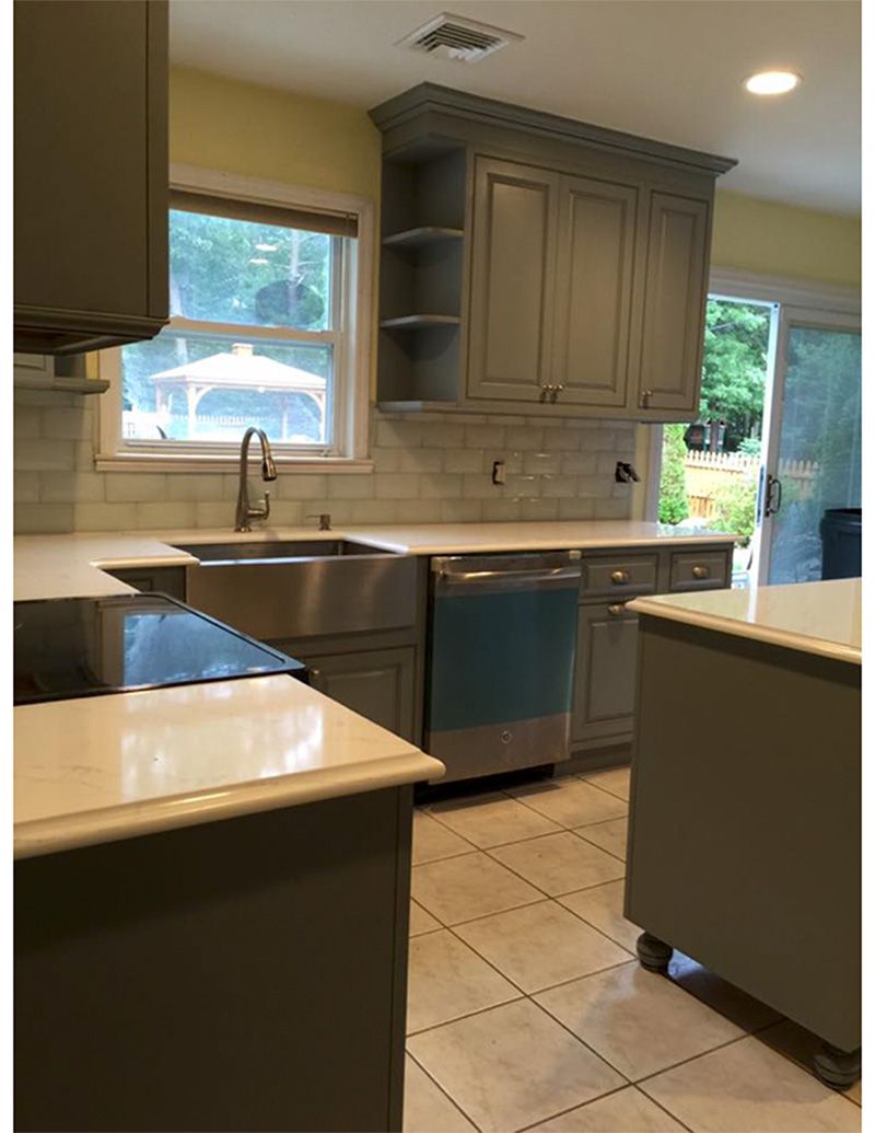 Kitchen with gray cabinets, stainless steel sink and appliances, white countertops, and a sliding glass door.