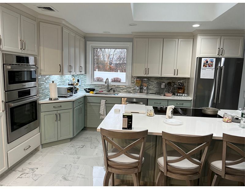 Kitchen with white and green cabinets, stainless steel appliances, and a central island with bar stools.