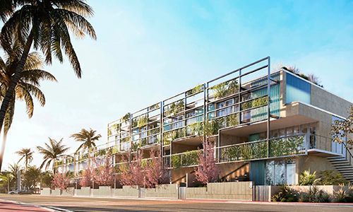 Modern glass-fronted apartment building with balconies and palm trees along a sunny street