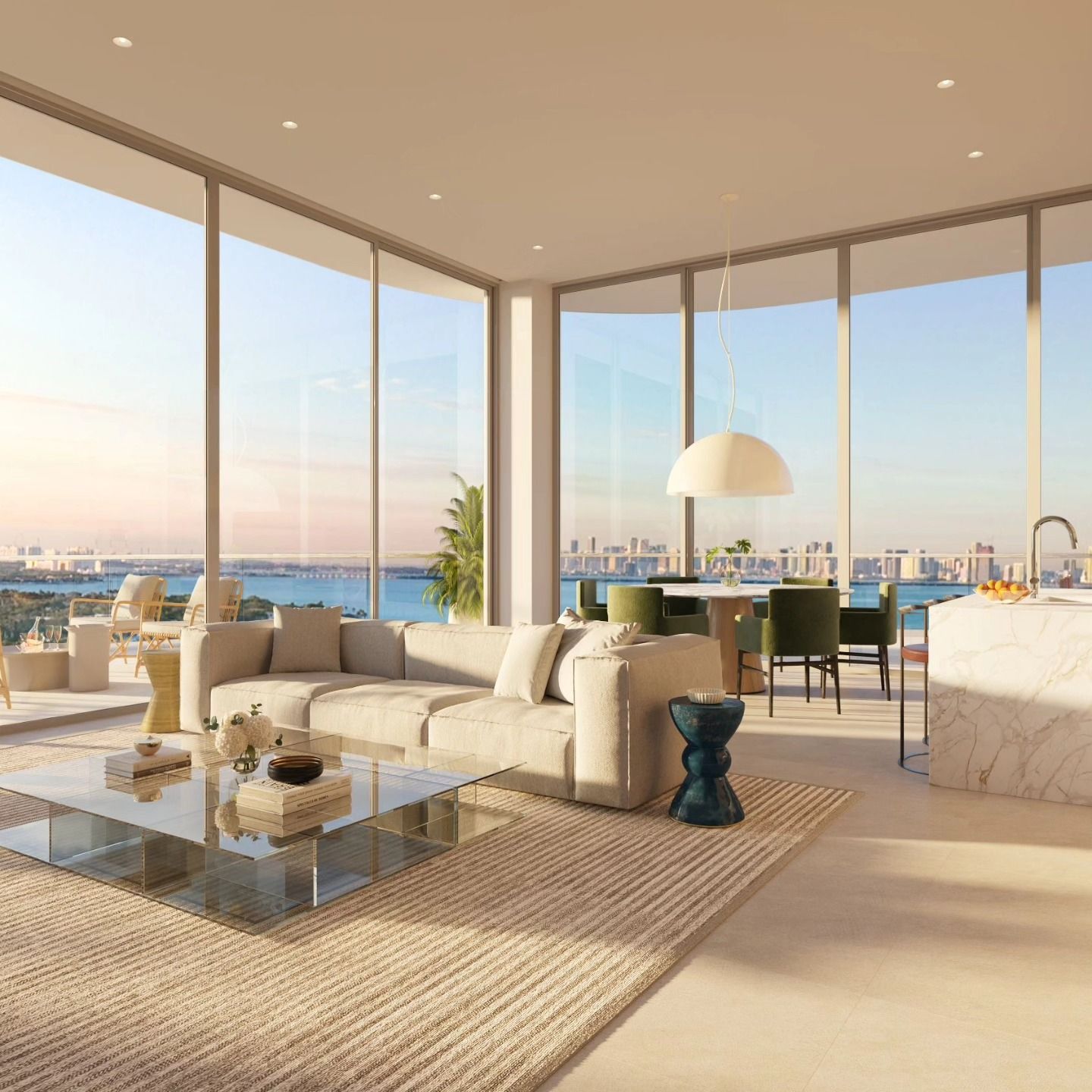 Modern living room with cream furniture, glass coffee table, and ocean-view windows at sunset.